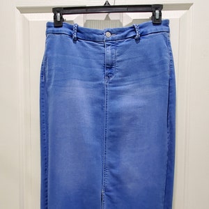 May include: A blue denim skirt with a front slit and a button closure. The skirt is hanging on a hanger.