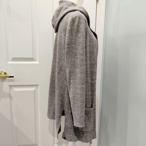 Pode incluir: Um cardigan cinza com capuz, mangas compridas e dois bolsos frontais. O cardigan &eacute; feito de um material macio e texturizado e tem um ajuste descontra&iacute;do. A bainha apresenta fendas laterais.