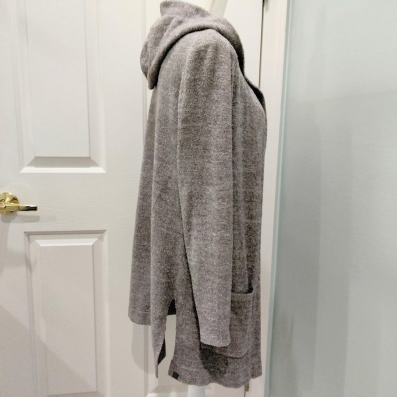Pode incluir: Um cardigan cinza com capuz, mangas compridas e dois bolsos frontais. O cardigan &eacute; feito de um material macio e texturizado e tem um ajuste descontra&iacute;do. A bainha apresenta fendas laterais.