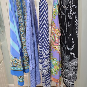 May include: A clothing rack displaying five dresses. The dresses are various colors and patterns, including blue, purple, and black. The rack is white and stands on a tiled floor.