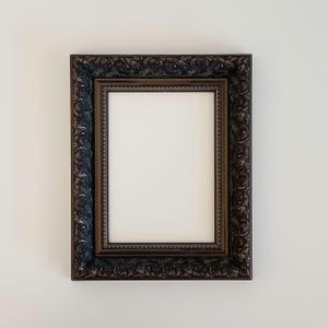 May include: A dark brown ornate picture frame with a white mount and a blank white space inside. The frame has a decorative, intricate design.