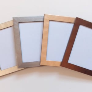 May include: Four picture frames in different colours: gold, silver, brown, and beige. The frames are all the same size and shape, and they are arranged in a row.