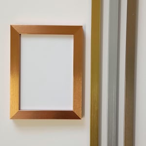 May include: A gold picture frame with a white mount and a white background. The frame is made of metal and has a brushed finish. The frame is 20.3 cm by 25.4 cm.