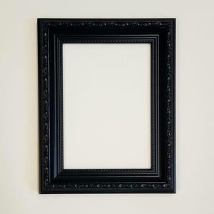 May include: A black rectangular picture frame with decorative detailing. The frame has a glossy finish and a traditional design. The frame is empty, with a white interior, ready for a photo or artwork.