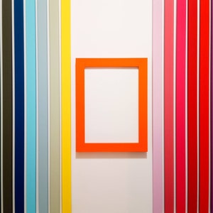May include: A bright orange picture frame against a white wall with a colourful vertical stripe pattern on either side.