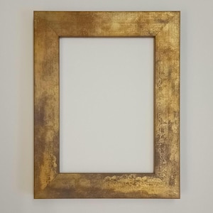 May include: A rectangular gold picture frame with a textured surface. The frame has a wide border and a white interior, suitable for displaying artwork or photographs. The frame is made of wood.