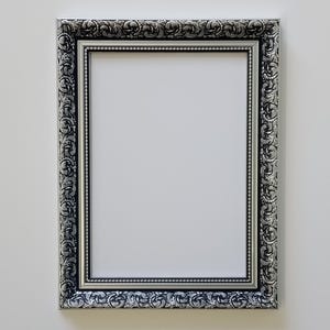May include: A silver picture frame with an ornate design and a black mount. The frame is empty.