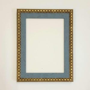 May include: A rectangular picture frame with a gold beaded border and a light blue inner frame. The frame has a white interior, ready for a photo or artwork. The frame is displayed against a white wall.