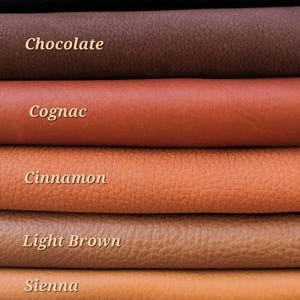 May include: A close-up of stacked leather swatches in various shades of brown. The colors range from dark brown to almond, with labels such as "Dark Brown", "Chocolate", "Cognac", "Cinnamon", "Light Brown", "Sienna", and "Almond".