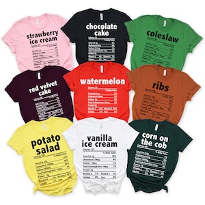 K&ouml;nnte beinhalten: Eine Auswahl an farbenfrohen T-Shirts, jedes mit einem Lebensmittelnamen und N&auml;hrwertangaben bedruckt. Die Shirts sind in verschiedenen Farben erh&auml;ltlich, darunter Rosa, Schwarz, Gr&uuml;n, Rot, Braun, Gelb, Wei&szlig; und Dunkelgr&uuml;n. Der Text ist fett und ohne Serifen.