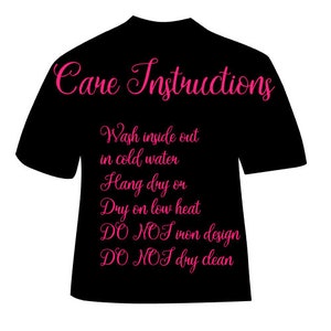 May include: Black t-shirt with pink text that reads "Care Instructions" and includes instructions for washing and drying the shirt. The instructions are: "Wash inside out in cold water, Hang dry or dry on low heat, DO NOT iron design, DO NOT dry clean."