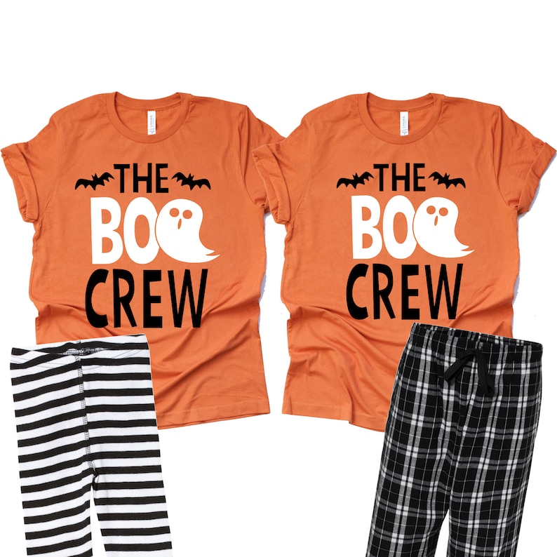 May include: Two orange t-shirts with the text "THE BOO CREW" and a ghost graphic, paired with black and white striped leggings and black and white plaid pajama pants. Halloween-themed apparel.