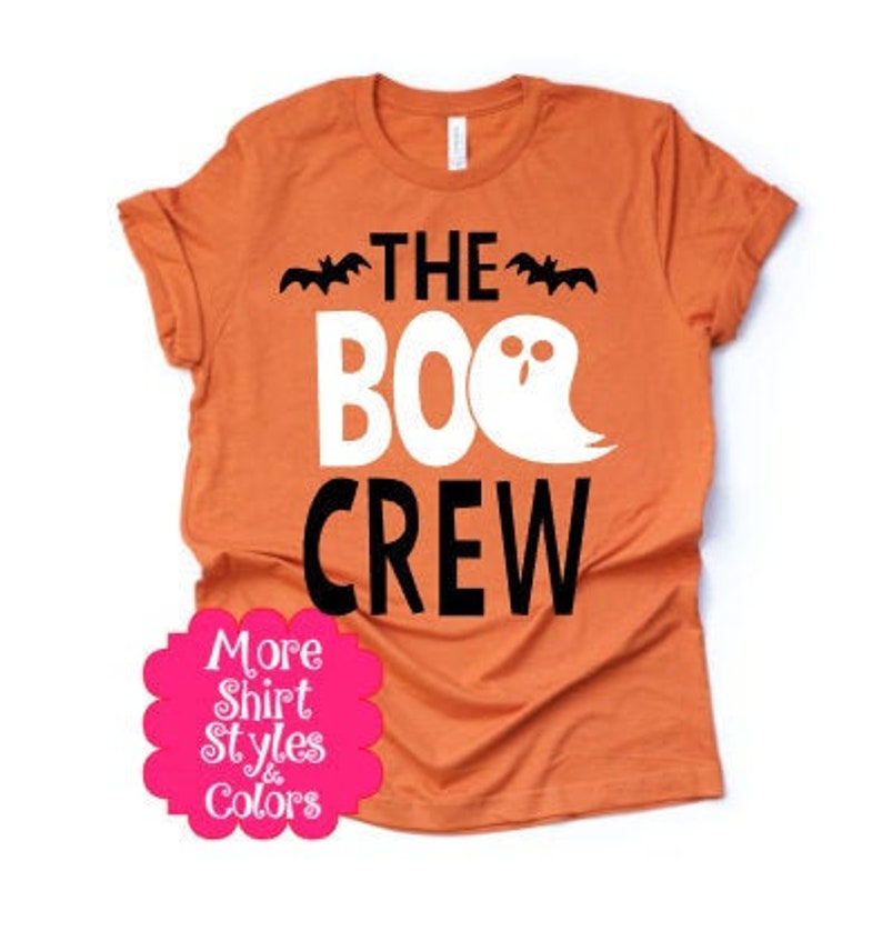 Pu&ograve; includere: T-shirt arancione con la scritta "THE BOO CREW" in bianco e nero. Il design include pipistrelli e un fantasma, perfetto per Halloween. Un adesivo rosa con testo in basso.