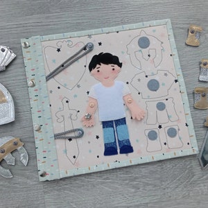 May include: A fabric activity board with a knight theme. The board features a felt figure of a boy with removable clothing pieces, including a helmet, armor, and sword. Additional felt knight accessories are scattered around the board.
