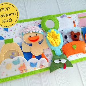 May include: A colorful felt quiet book with a bath time theme. Features a duck wearing a flower crown, a soap bottle, a mirror, a brush, and a frog. The book is bordered with green fabric and includes the text "PDF Pattern SVG".