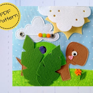 May include: A handmade felt quiet book page with a sunny day theme. Features a green tree, a brown tree, white clouds, and a yellow sun. The page has a blue background with white polka dots and green grass.