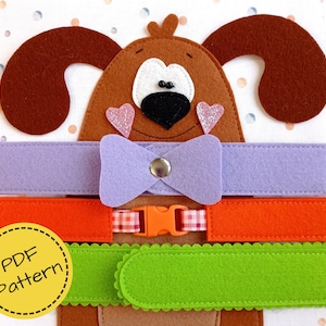 Op de afbeelding: Een educatief speelgoed in de vorm van een hond van vilt, met een bruin lichaam, oren en een wit gezicht. Het heeft een paarse kraag met een vlinderdas, een oranje kraag met een gesp en een groene kraag. De afbeelding bevat een label "PDF Pattern".
