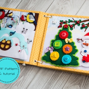 May include: A handmade felt quiet book with winter and Christmas scenes. The pages feature a snowy landscape with birds, a house, and a Christmas tree decorated with colorful buttons. The book is bound with a yellow polka dot fabric.