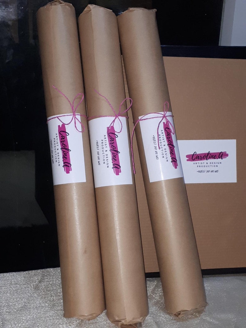 Pode incluir: Tr&ecirc;s tubos de papel castanho com um cord&atilde;o rosa amarrado &agrave; volta. Cada tubo tem um r&oacute;tulo branco com o texto "Caroline A" e "Artist & Design Production" em preto.