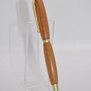 May include: A wooden pen with gold accents. The pen has a striped wood pattern and a gold clip.