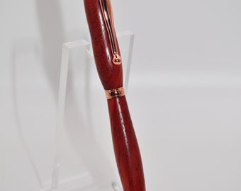May include: A wooden pen with a copper finish. The pen has a dark red wood grain and a copper clip and tip.