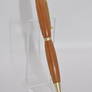 May include: A wooden pen with gold accents. The pen has a brown and light brown striped pattern. The pen is displayed on a clear acrylic stand.