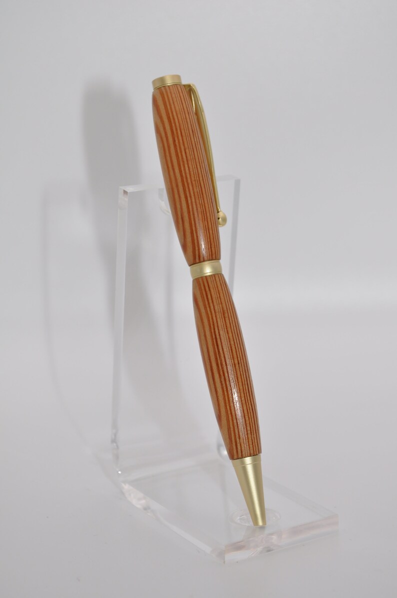 May include: A wooden pen with gold accents. The pen has a brown and light brown striped pattern. The pen is displayed on a clear acrylic stand.