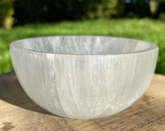 May include: A white selenite bowl with a smooth, polished surface. The bowl is made of natural selenite crystal and has a unique, organic shape.