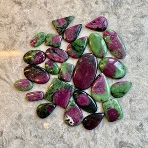 May include: A collection of 20 green and pink gemstone cabochons. The stones are various shapes and sizes, with some having a more opaque appearance and others being more translucent.