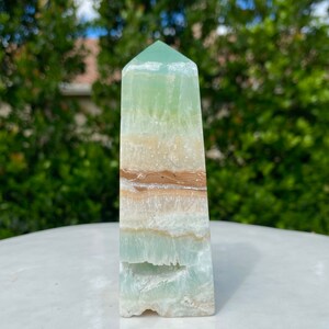 May include: A green, white, and brown banded crystal point. The crystal is polished and has a smooth, glassy surface.