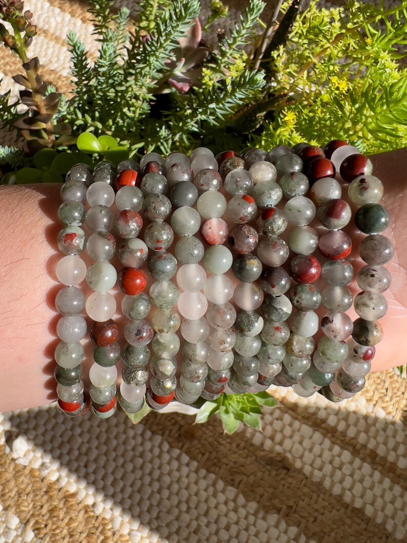 Pu&ograve; includere: Un set di braccialetti realizzati con perline di pietre preziose verdi, rosse e bianche. I braccialetti sono impilati sul polso di una persona.