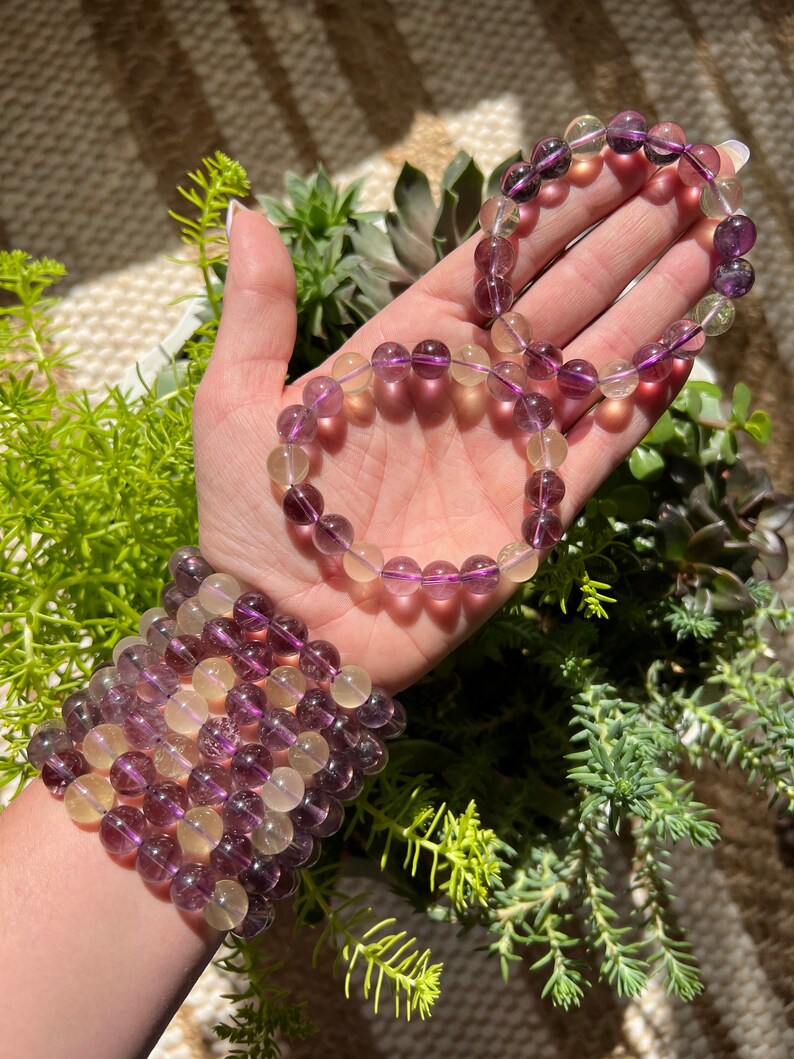 Puede incluir: Un conjunto de tres pulseras hechas con cuentas de fluorita p&uacute;rpura y amarilla. Las pulseras est&aacute;n apiladas en la mu&ntilde;eca de una persona.