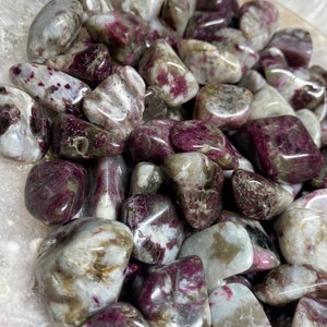May include: A collection of tumbled pink and white stones with a speckled pattern. The stones are smooth and polished, and they have a natural, organic look.