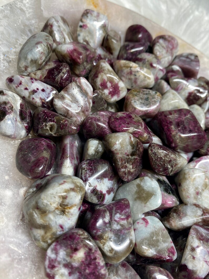 May include: A collection of tumbled pink and white stones with a speckled pattern. The stones are smooth and polished, and they have a natural, organic look.