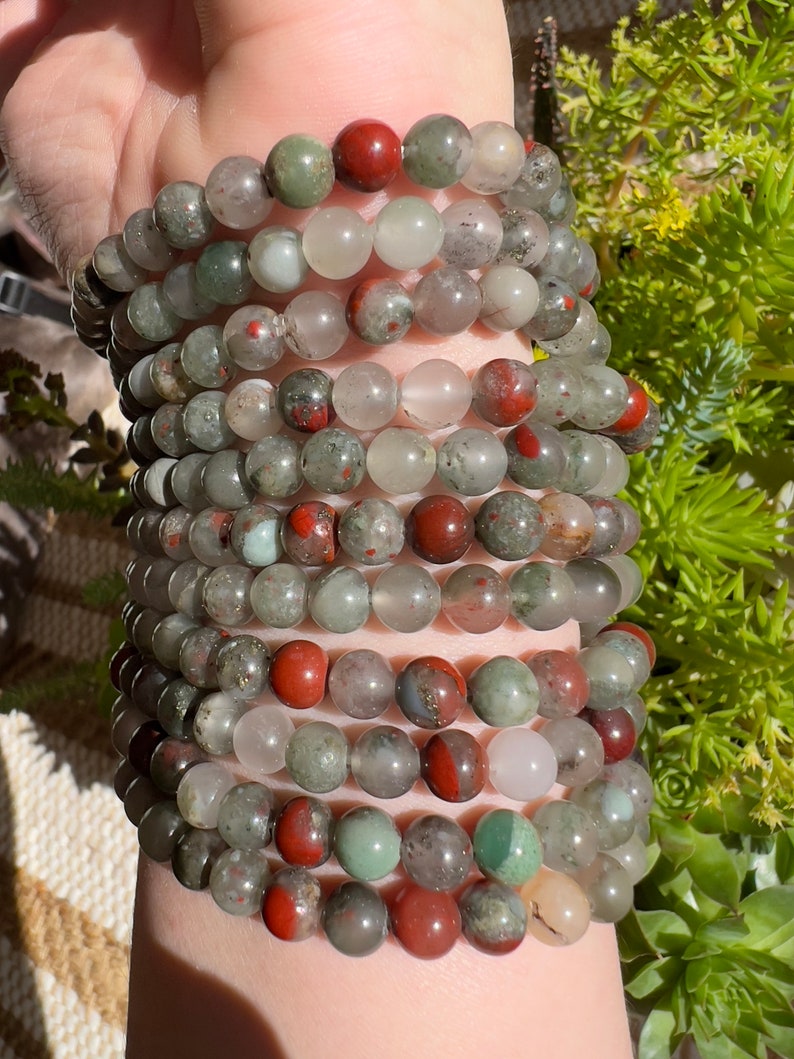 Pu&ograve; includere: Un set di braccialetti realizzati con perline di pietre preziose verdi, rosse e bianche. I braccialetti sono sovrapposti sul polso di una persona.