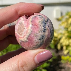 May include: A pink and gray sphere of polished pink manganese, also known as rhodochrosite, with a swirling pattern of pink, white, and gray.