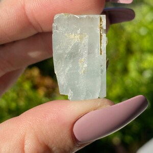 May include: A light blue aquamarine crystal with a golden inclusion. The crystal is faceted and has a rectangular shape.