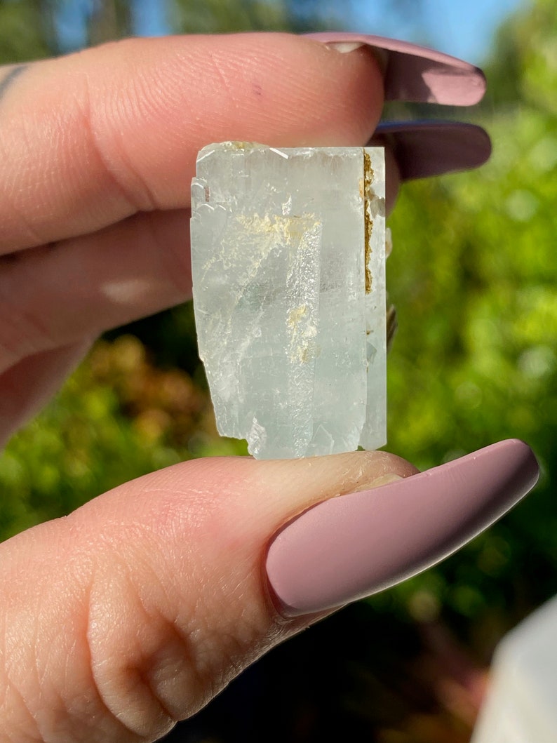 May include: A light blue aquamarine crystal with a golden inclusion. The crystal is faceted and has a rectangular shape.