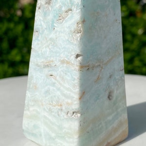May include: A light blue and white celestite crystal pyramid with a smooth, polished surface. The crystal has a natural, organic pattern of white and light blue swirls.
