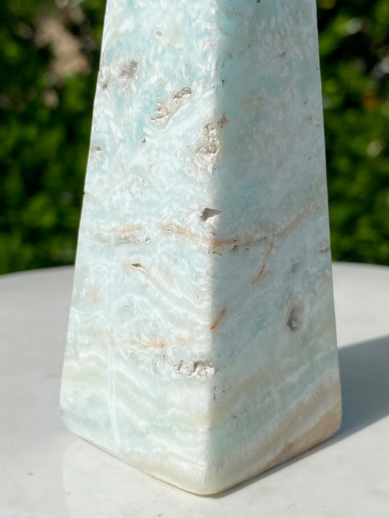 May include: A light blue and white celestite crystal pyramid with a smooth, polished surface. The crystal has a natural, organic pattern of white and light blue swirls.