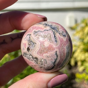 May include: A pink and black sphere of polished  pink  and black  stone. The sphere has a swirling pattern of pink and black.