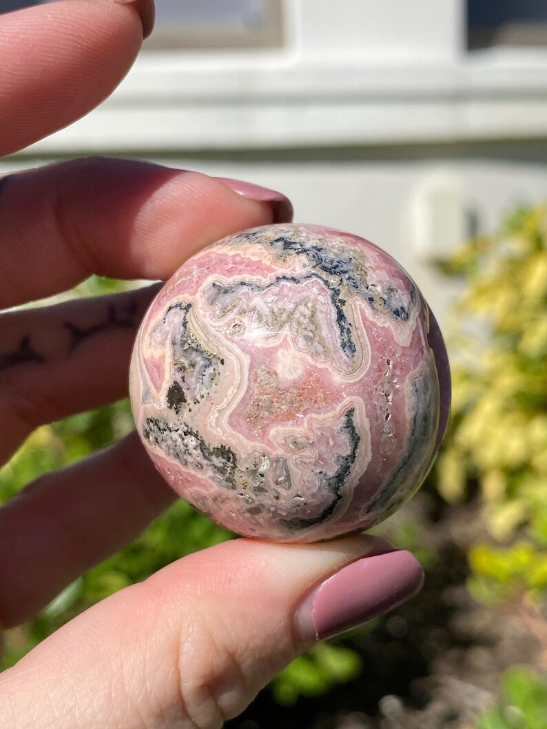 May include: A pink and black sphere of polished  pink  and black  stone. The sphere has a swirling pattern of pink and black.
