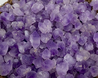 May include: A woven basket filled with numerous raw amethyst crystals. The crystals vary in size and shape, displaying a range of purple hues. The basket's natural brown color contrasts with the vibrant purple of the gemstones.