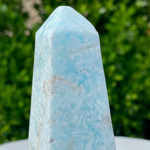 May include: A light blue, naturally formed, crystal point with a swirling, marbled pattern. The crystal is polished and has a smooth, glassy surface.