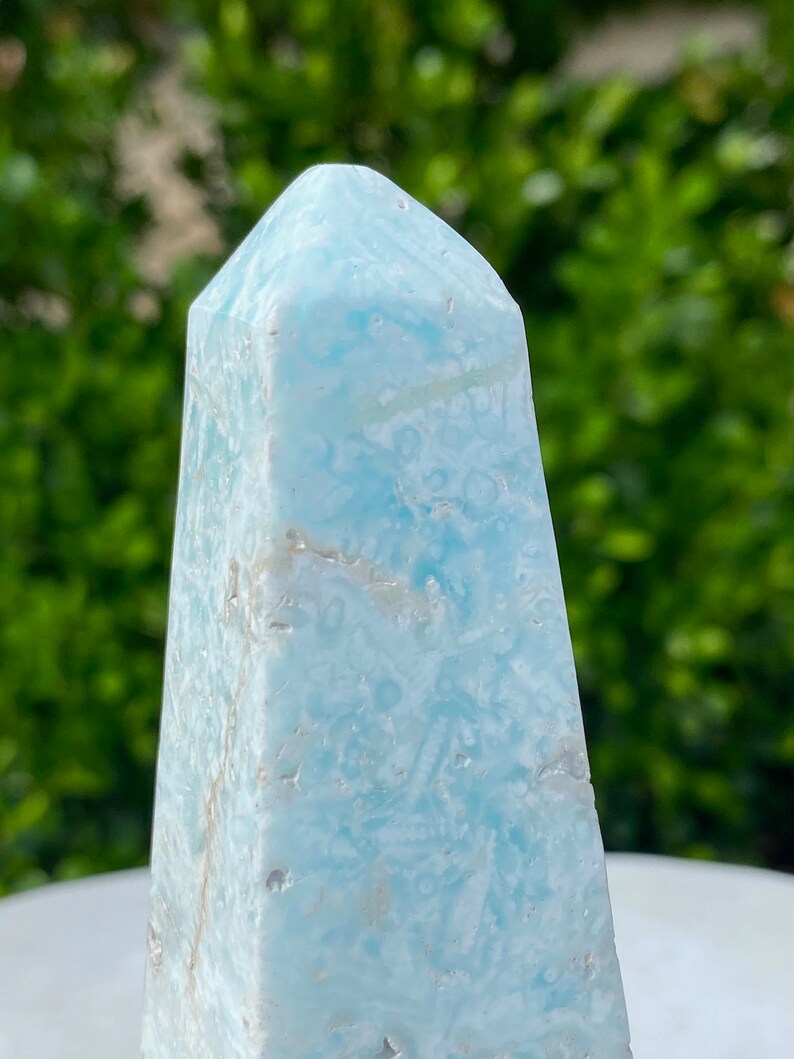 May include: A light blue, naturally formed, crystal point with a swirling, marbled pattern. The crystal is polished and has a smooth, glassy surface.