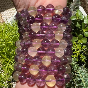Puede incluir: Un brazalete hecho de cuentas de piedras preciosas de color p&uacute;rpura y amarillo alternadas. Las cuentas son redondas y tienen un acabado liso y pulido.