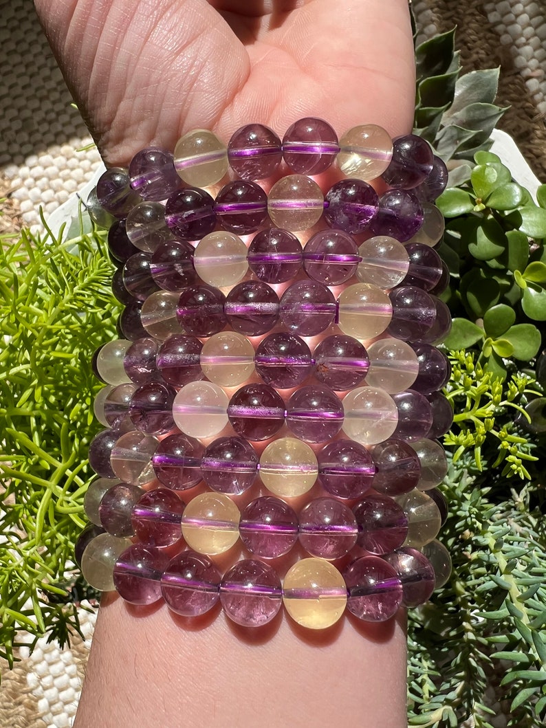 Puede incluir: Un brazalete hecho de cuentas de piedras preciosas de color p&uacute;rpura y amarillo alternadas. Las cuentas son redondas y tienen un acabado liso y pulido.