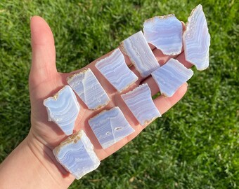 May include: A collection of blue agate slices with white and brown banding. The slices are various shapes and sizes and are arranged on a hand.