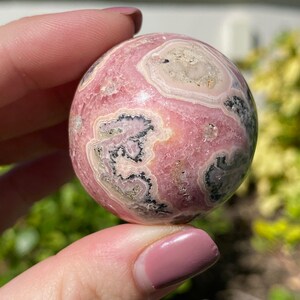 May include: A pink and white sphere with black and grey swirls. The sphere is made of polished stone and has a smooth, glossy finish.