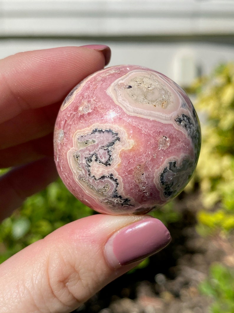 May include: A pink and white sphere with black and grey swirls. The sphere is made of polished stone and has a smooth, glossy finish.